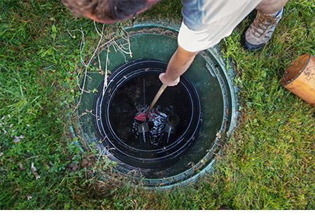 Overhead view of a septic technician inspecting the wastewater and pipes in a septic tank.