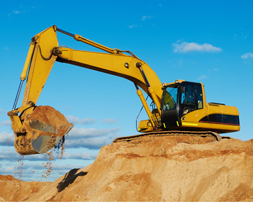 Large yellow excavator scooping sand out of a pit and loading it into a dump truck for shipping.