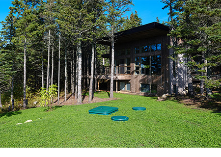 Depuradora con biofiltro Ecoflo instalada en una vivienda unifamiliar con árboles y césped verde.