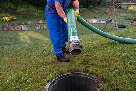 Vidangeur de fosse septique qui insère un tuyau d’aspiration dans une fosse septique pour éliminer les boues et maintenir la performance du système.