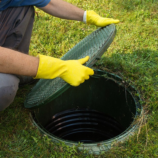 Homme avec des gants de protection qui ouvre un couvercle vert de fosse septique.