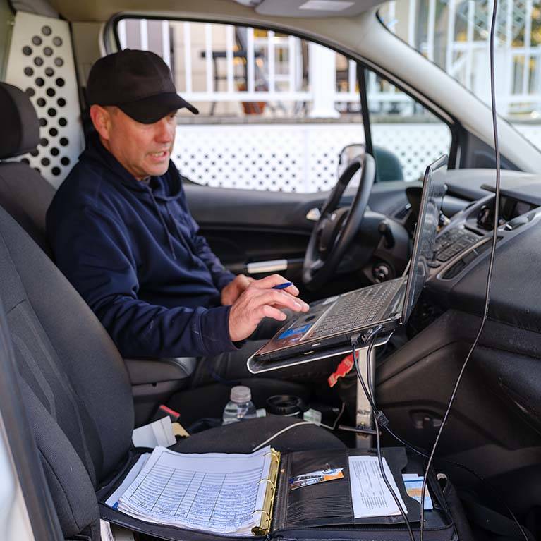 Technicien finalisant le rapport de visite sur son ordinateur portable, dans sa voiture.