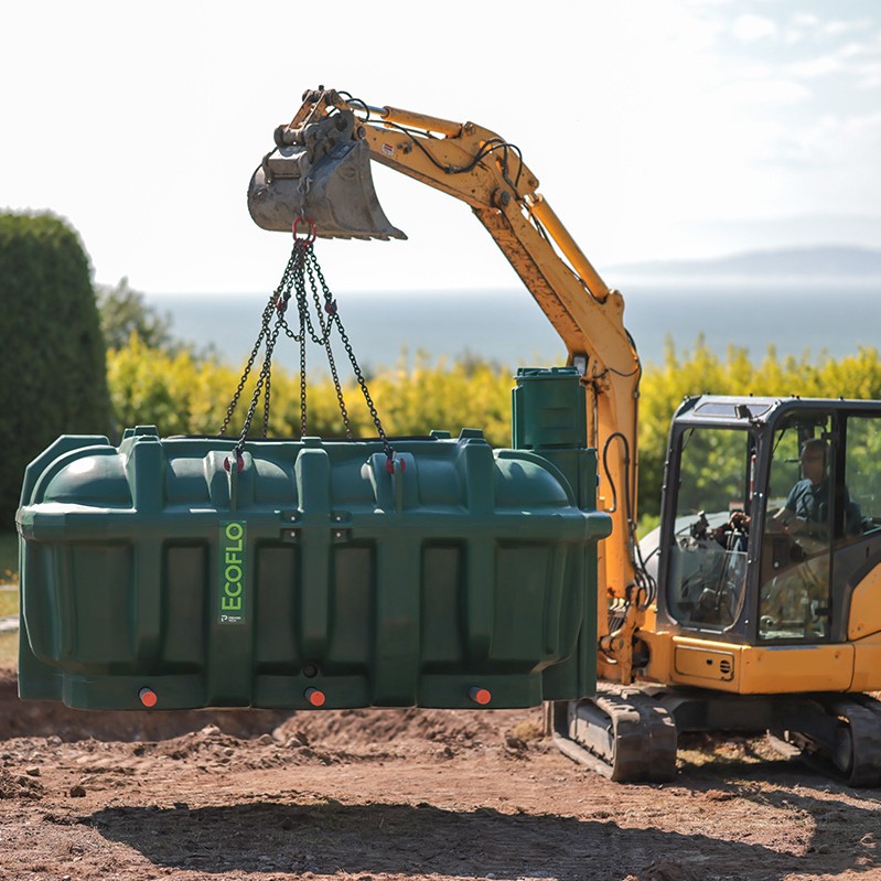 Backhoe lifting the polyethylene Ecoflo biofilter into an excavation on a rural property with a small lot.