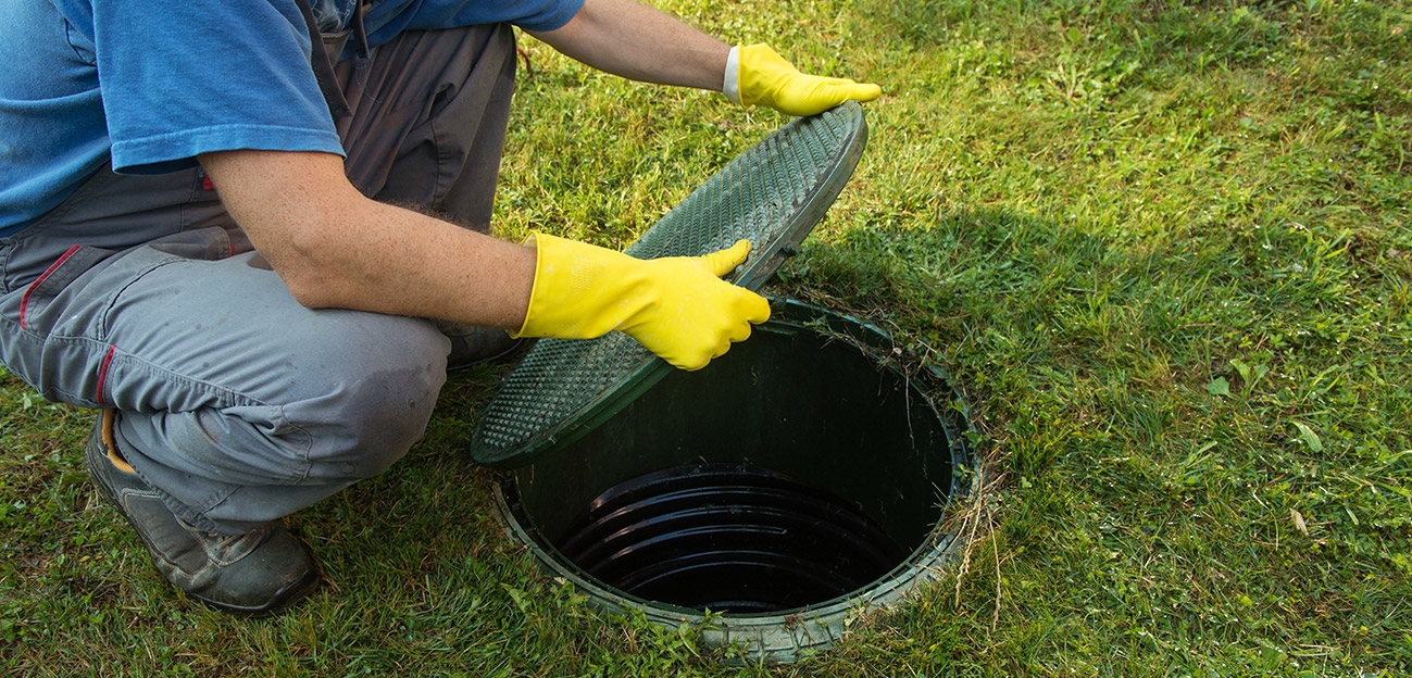 Homme avec des gants de protection qui ouvre un couvercle vert de fosse septique.