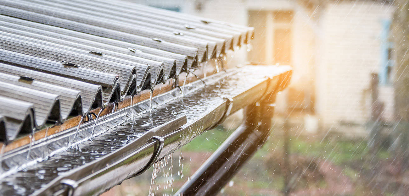 Regn faller på ett korrugerat plåttak och rinner in i en ränna som är ansluten till ett system för uppsamling av regnvatten.