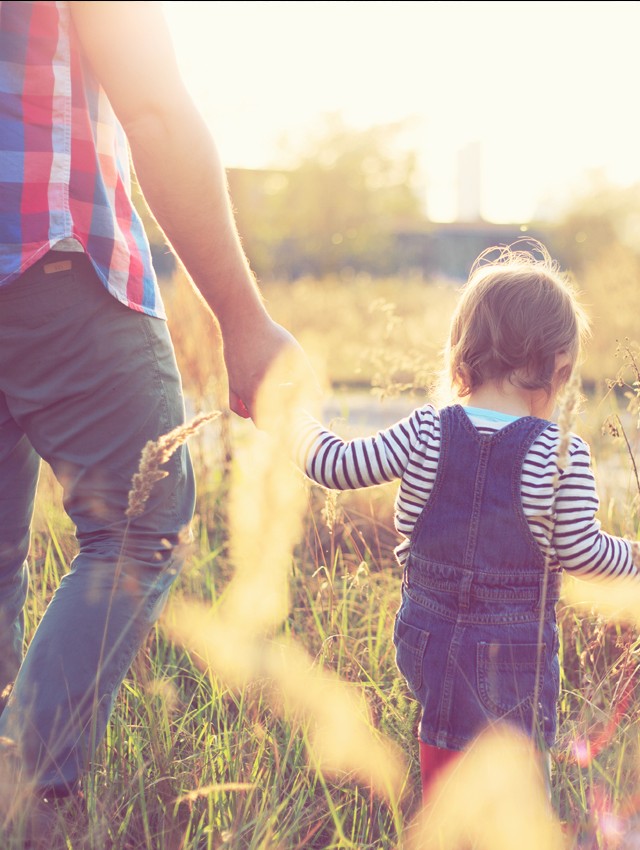 Child holding hands with his father as they walk through a field.