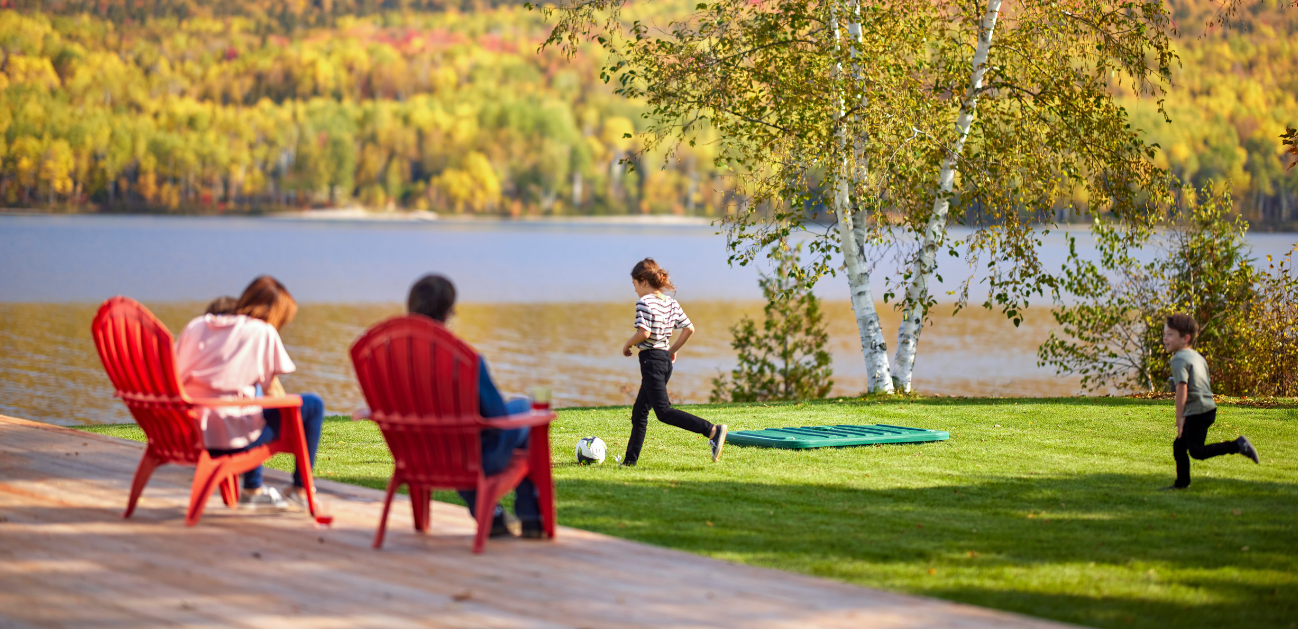 Famille relaxant sur le bord d'un lac avec des enfants qui jouent au soccer près d'un couvercle de biofiltre Ecoflo sur la pelouse.