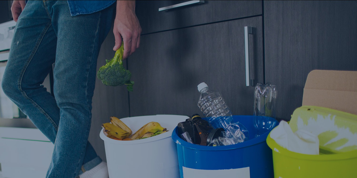 Man putting paper, plastic bottles, and organic waste into recycling bins in his kitchen.