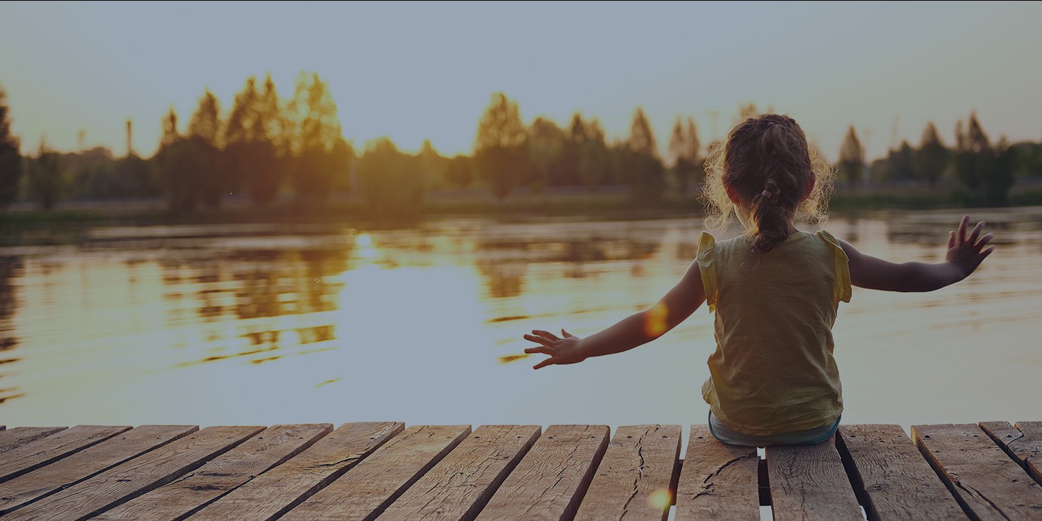 Young girl watching the sunset on a lake dock near a forest.