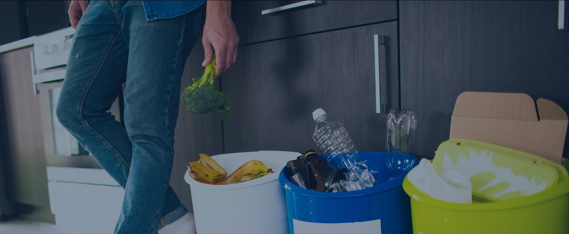 Man putting paper, plastic bottles, and organic waste into recycling bins in his kitchen.