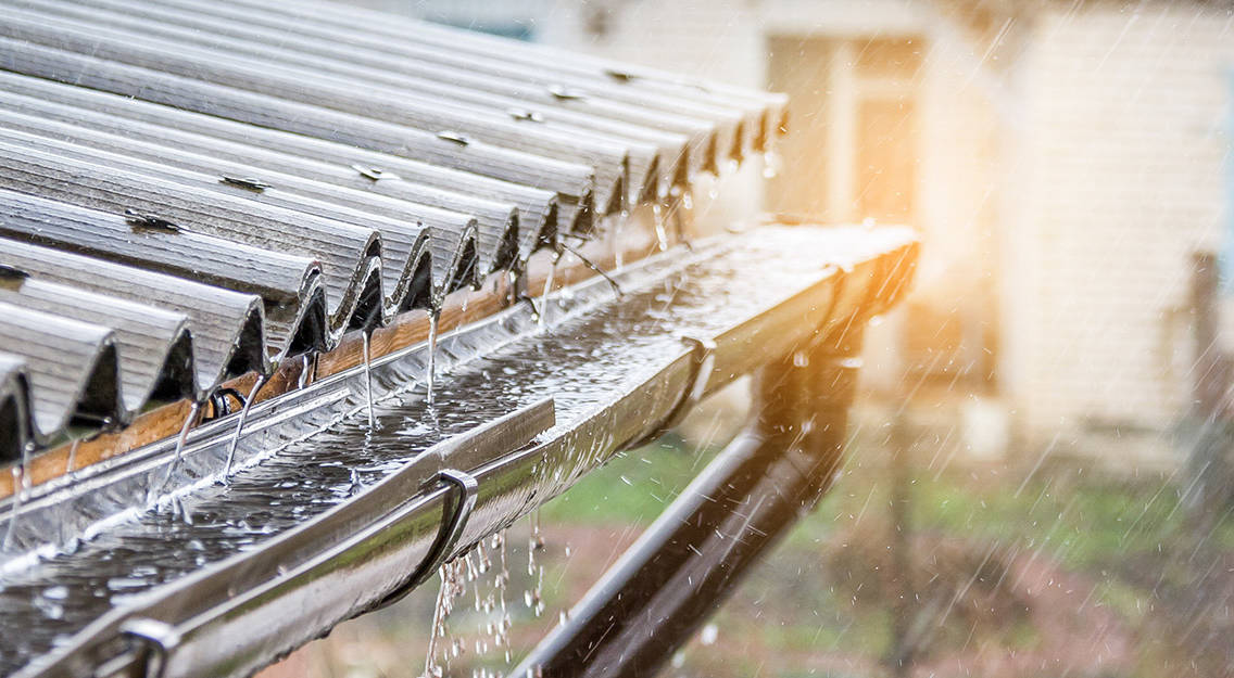 Regn faller på ett korrugerat plåttak och rinner in i en ränna som är ansluten till ett system för uppsamling av regnvatten.