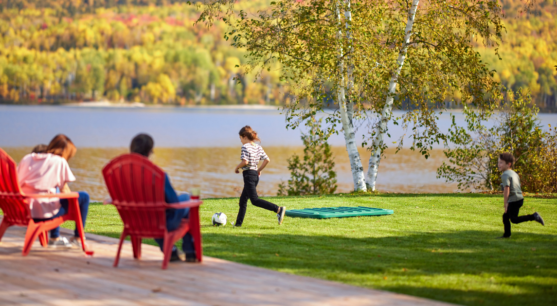 Famille relaxant sur le bord d'un lac avec des enfants qui jouent au soccer près d'un couvercle de biofiltre Ecoflo sur la pelouse.