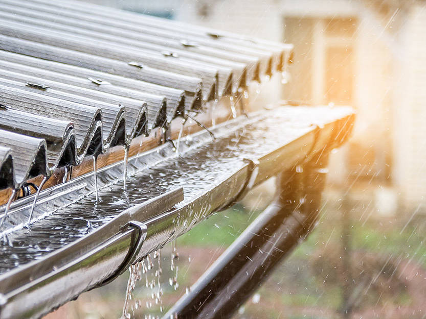 Rain falling on a corrugated metal roof and flowing into a gutter connected to a rainwater harvesting system.