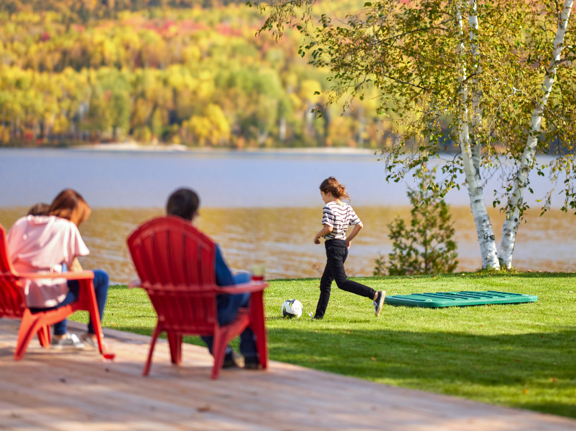 Famille relaxant sur le bord d'un lac avec des enfants qui jouent au soccer près d'un couvercle de biofiltre Ecoflo sur la pelouse.