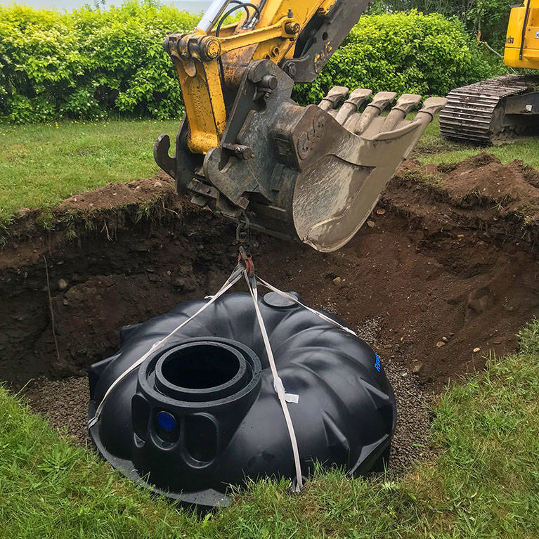 Excavateur mettant en terre le récupérateur d’eau de pluie souterrain de 3 000 litres de Premier Tech Eau et Environnement dans une cour résidentielle.