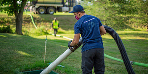 Man using a vacuum truck to pump the used filtering medium from an Ecoflo biofilter green septic system.