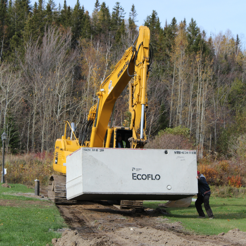 Excavateur déplaçant une cuve du biofiltre Ecoflo en béton.